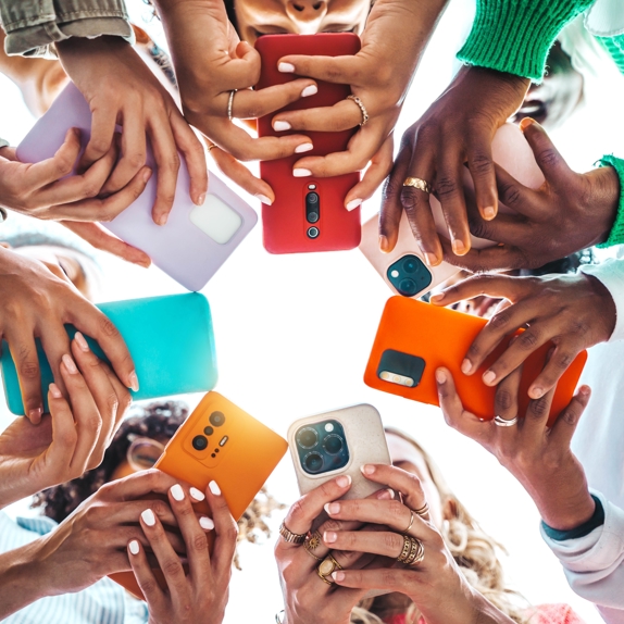 Fotoğrafta, daire şeklinde duran yedi kişi, başlarını eğmiş, göğüs hizasında tuttukları telefonlarla ilgileniyor.  Aşağıdan çekilmiş fotoğrafta, ellerinin arasındaki telefonlardan kişilerin yüzleri görünmüyor.