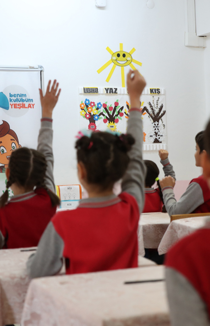 İlkokul çağındaki ikisi kız, ikisi erkek dört çocuk, yemyeşil bir kırda el ele tutuşarak çember olmuş, elleri havada neşeyle dönüyor. Fotoğrafın sol kısmında, kalın puntolu küçük beyaz harflerle dört satır halinde şu ifade yer alıyor: “Türkiye’nin en kapsamlı ve en yaygın bağımlılık önleme programı.” Devamında, ince puntolu küçük beyaz harflerle iki satır halinde şunlar yazıyor: “Bağımlılıklarla mücadelede yeni çözümler üretiyor, toplumu bilinçlendirmeye devam ediyoruz.”